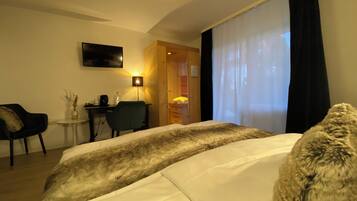 Habitación de hotel con cama, escritorio, silla, televisor y ventana con cortinas.