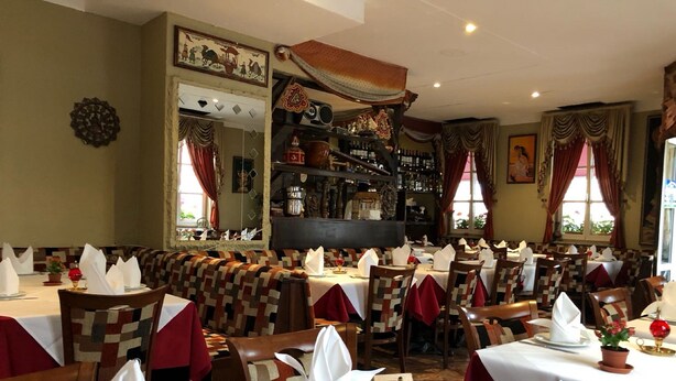 A restaurant with multiple tables set for dining, a bar area, and a seating area with patterned cushions. - Pension Mona Lisa (Munich)