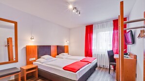 A modern hotel room with a large bed, a desk, a chair, a TV, and a mirror. - Hotel Am Friedensplatz (Stuttgart)