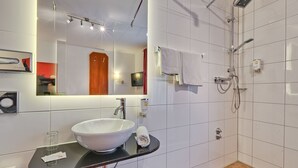 A modern bathroom with a large mirror, a white sink, a handheld showerhead, and a towel rack. - Hotel Am Friedensplatz (Stuttgart)