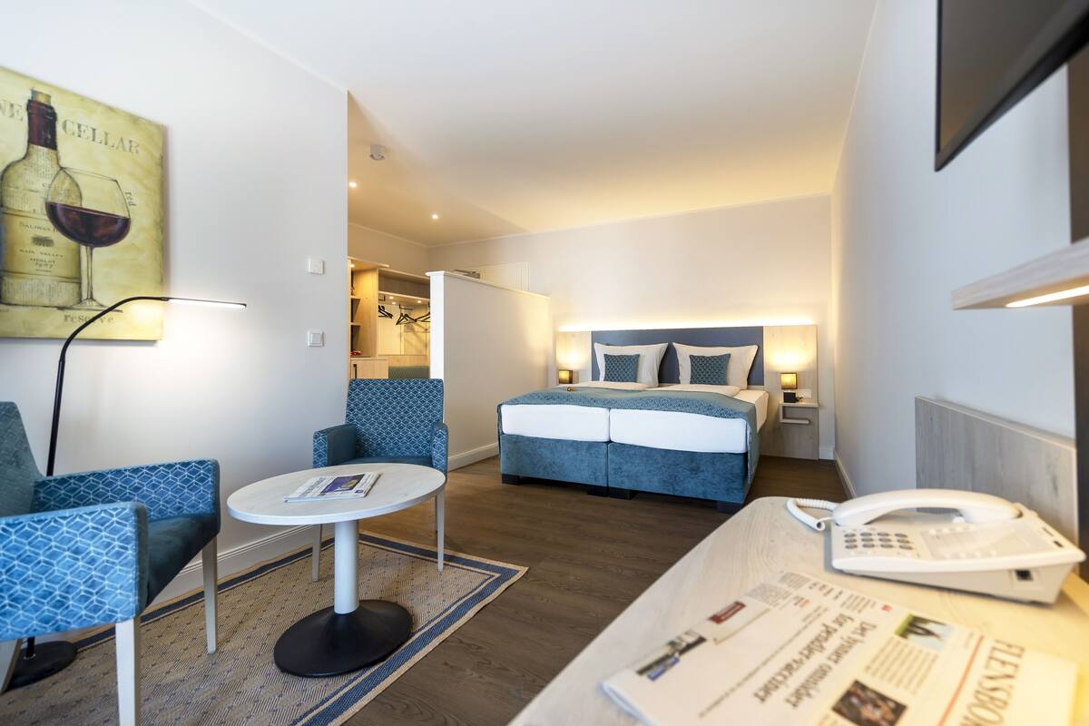 Ein Hotelzimmer mit einem Bett, zwei Stühlen, einem kleinen Tisch, einer Lampe und einem Telefon.