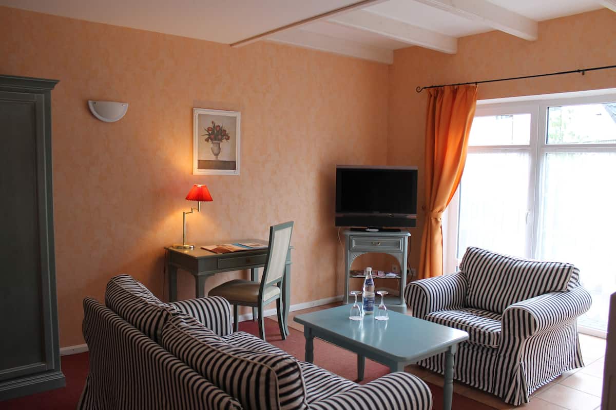 Ein Zimmer mit gestreiften Sofas, einem Tisch mit Gläsern, einem Fernseher und einem Schreibtisch mit Lampe.
