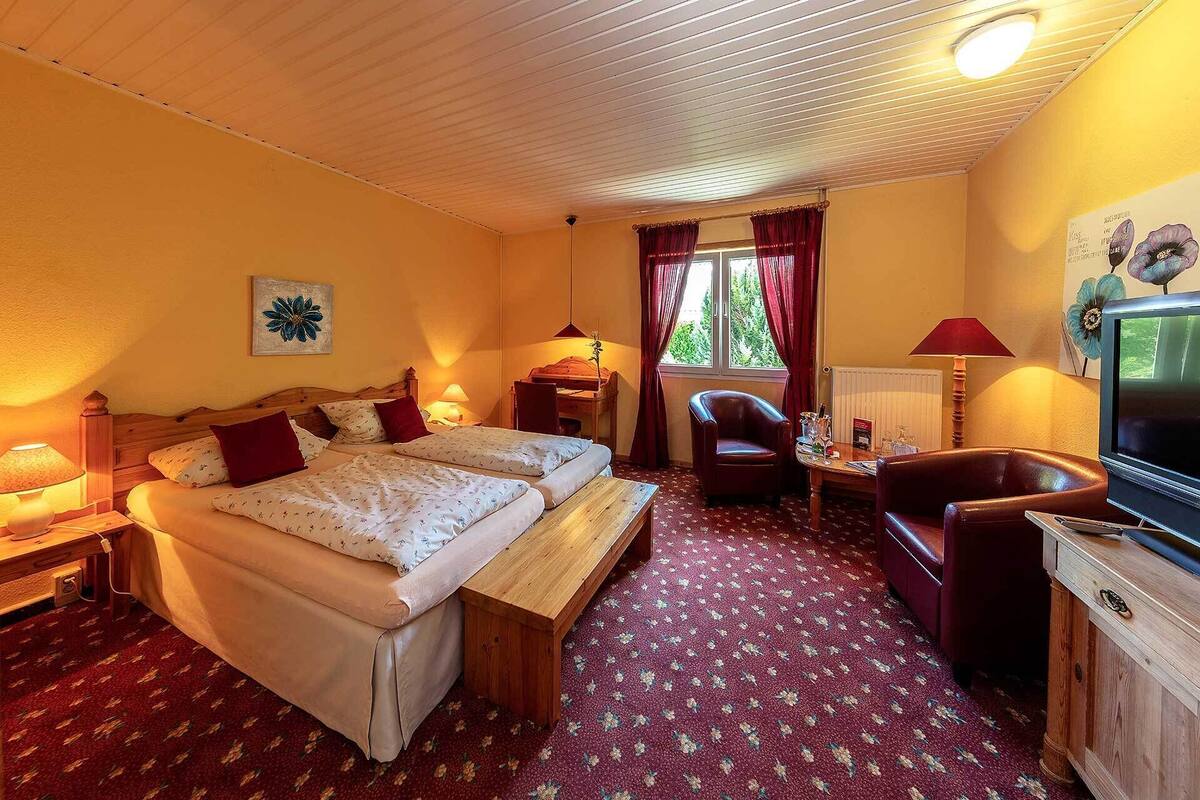 Ein Hotelzimmer mit zwei Betten, einem Schreibtisch, einem Fernseher und einem Fenster mit Vorhängen.