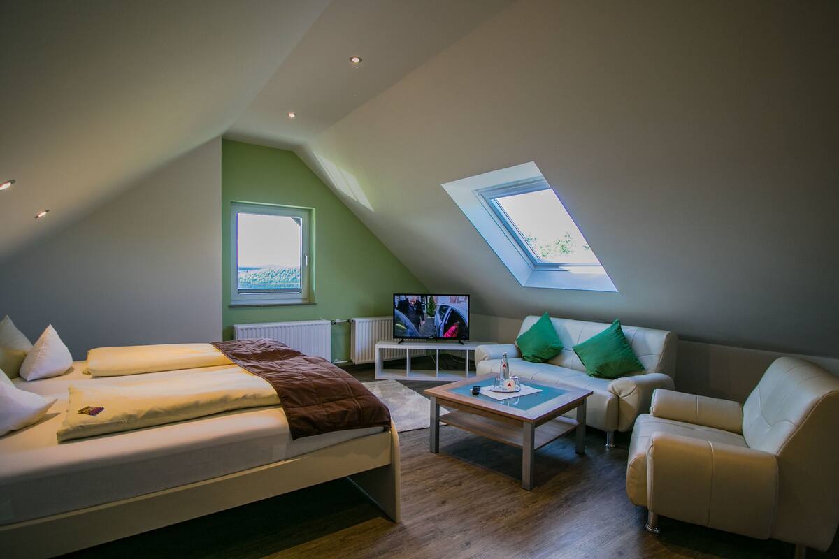A modern loft bedroom with a large bed, a sofa, and a TV.