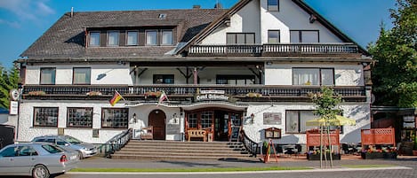 A two-story building with a balcony, a sign reading "Hotel Schneider," and a flag.