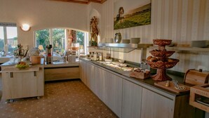 Una mesa de buffet con diversos alimentos y utensilios de servicio, una estatua decorativa y un cuadro con un paisaje en la pared.