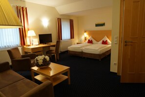 Une chambre d’hôtel comprenant un lit, un bureau avec un ordinateur, une chaise, une table avec un vase de fleurs et une lampe.