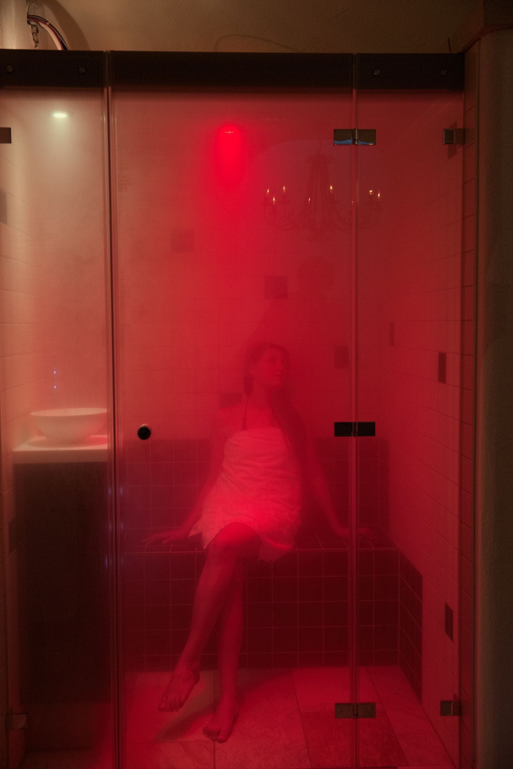 Una habitación con paredes de vidrio, una luz roja, un banco blanco y suelo de baldosas.
