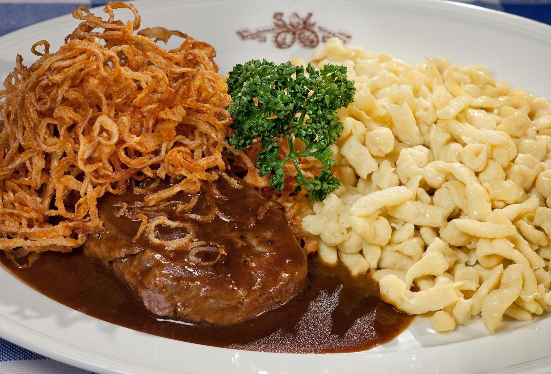 A plate with a meat dish, fried onions, and a side of noodles.