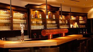 Een bar met houten barstoelen, planken met glaswerk en flessen.