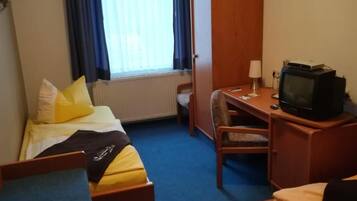 Ein Hotelzimmer mit zwei Einzelbetten, einem Schreibtisch mit Fernseher und einem Fenster mit Vorhängen.