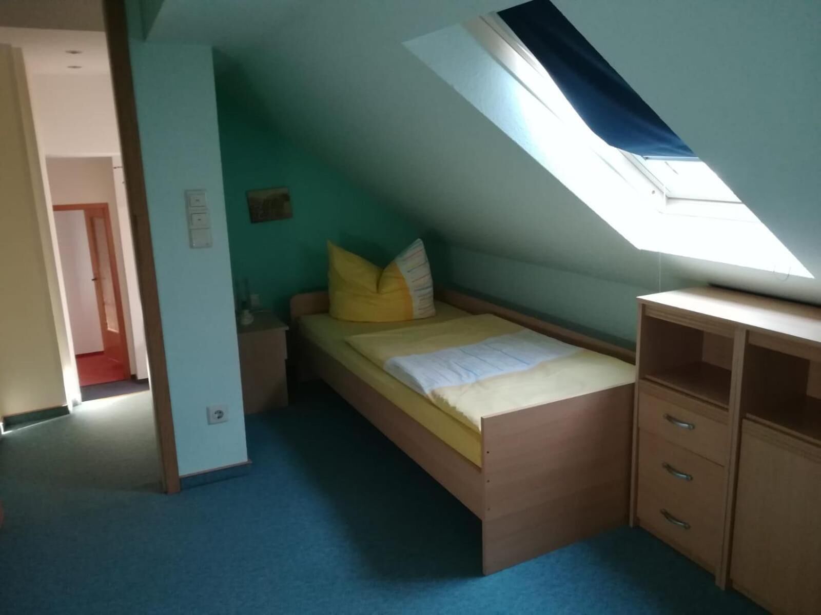 A small, single-bed room with a slanted ceiling and a skylight.