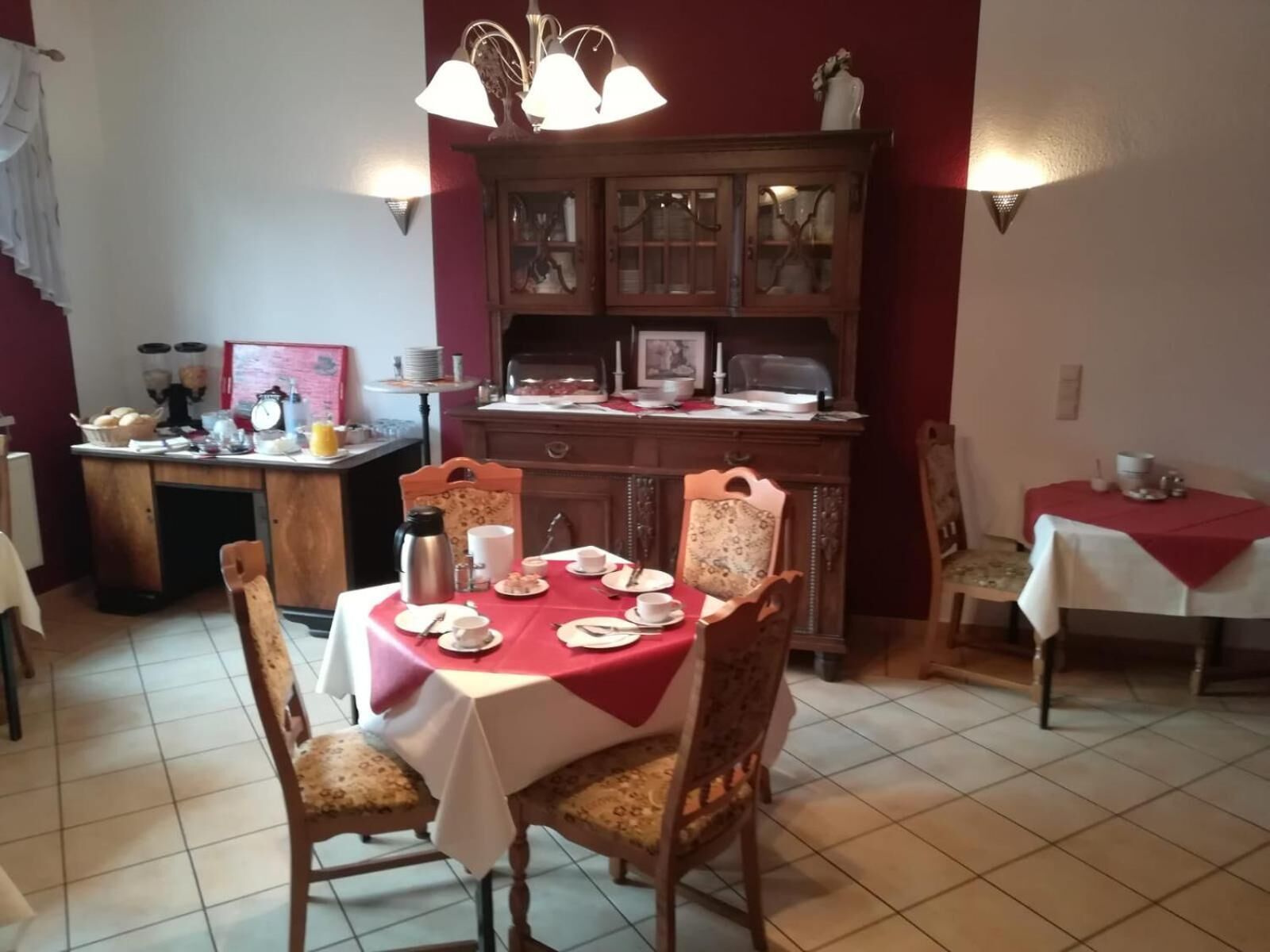 Un comedor con una mesa preparada para cuatro personas, un armario de madera con puertas de vidrio y una araña.