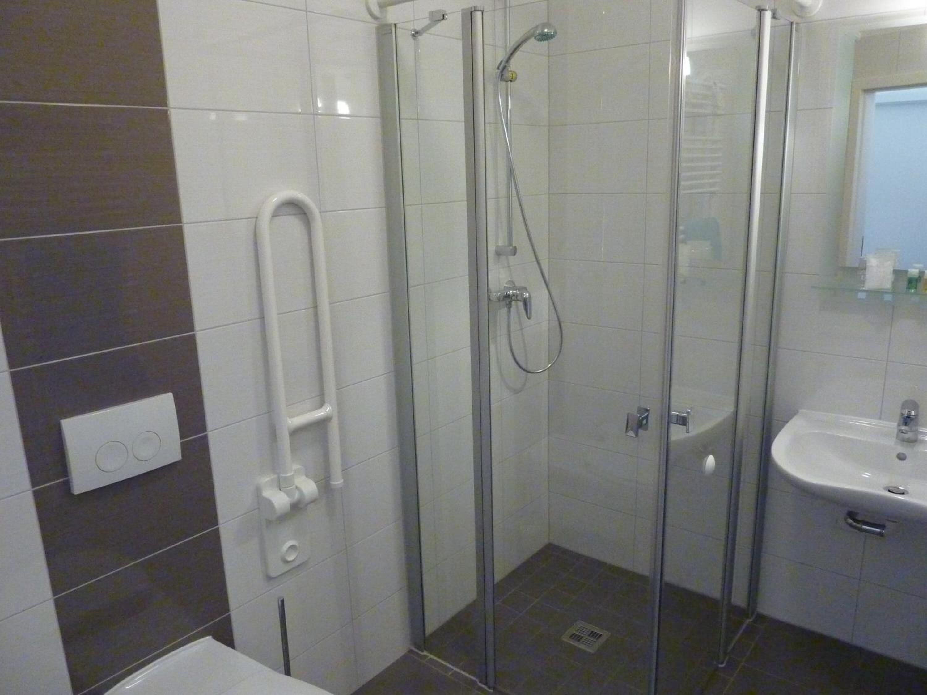 Een moderne badkamer met een douchecabine van glas, een witte wastafel en een toilet.