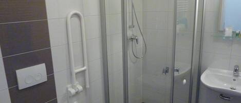 Een moderne badkamer met een douchecabine van glas, een witte wastafel en een toilet.