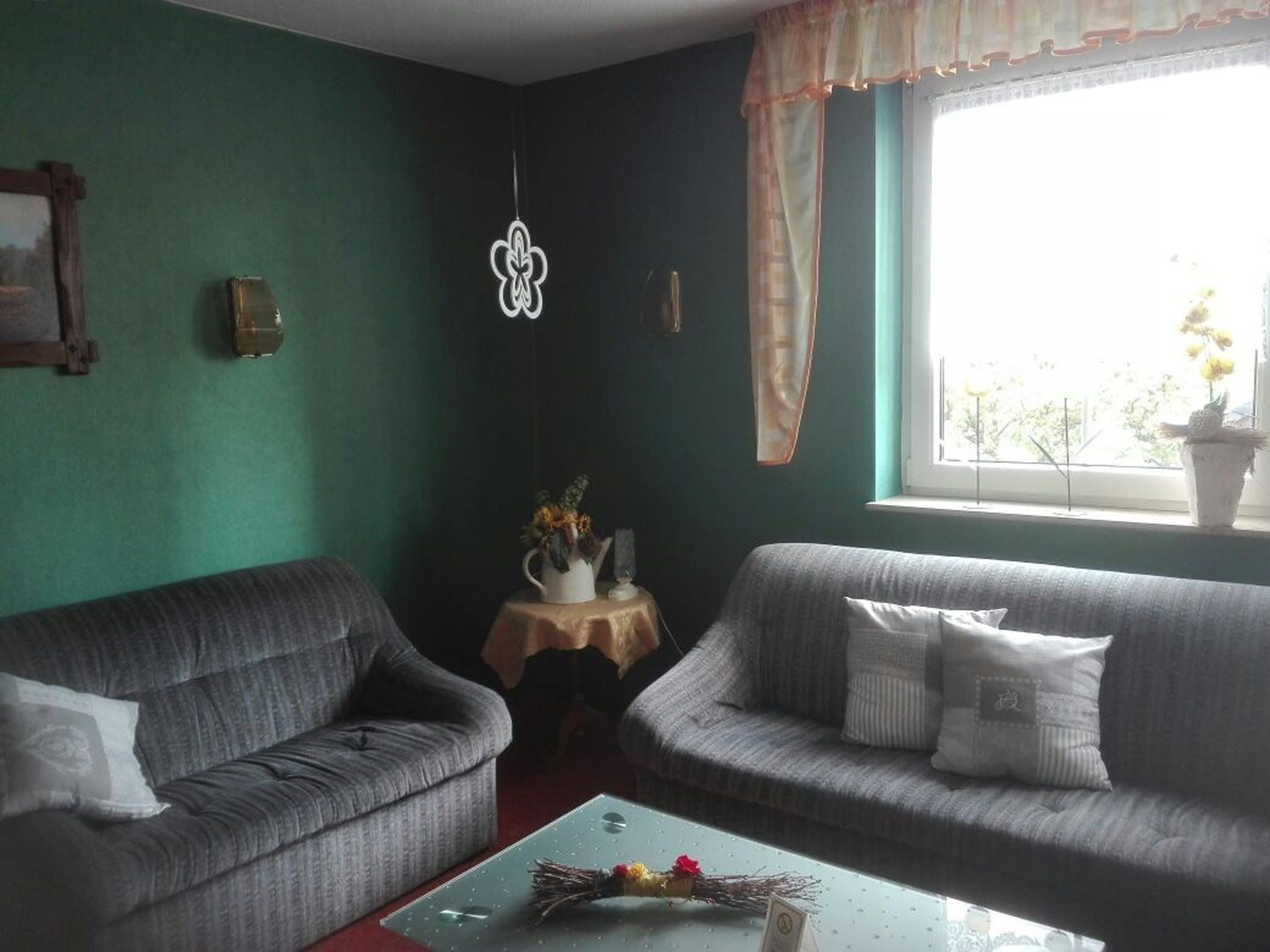 Ein Wohnzimmer mit zwei grauen Sofas, einem kleinen Tisch mit einer Vase und einer Kerze, sowie einem Fenster mit Vorhängen.