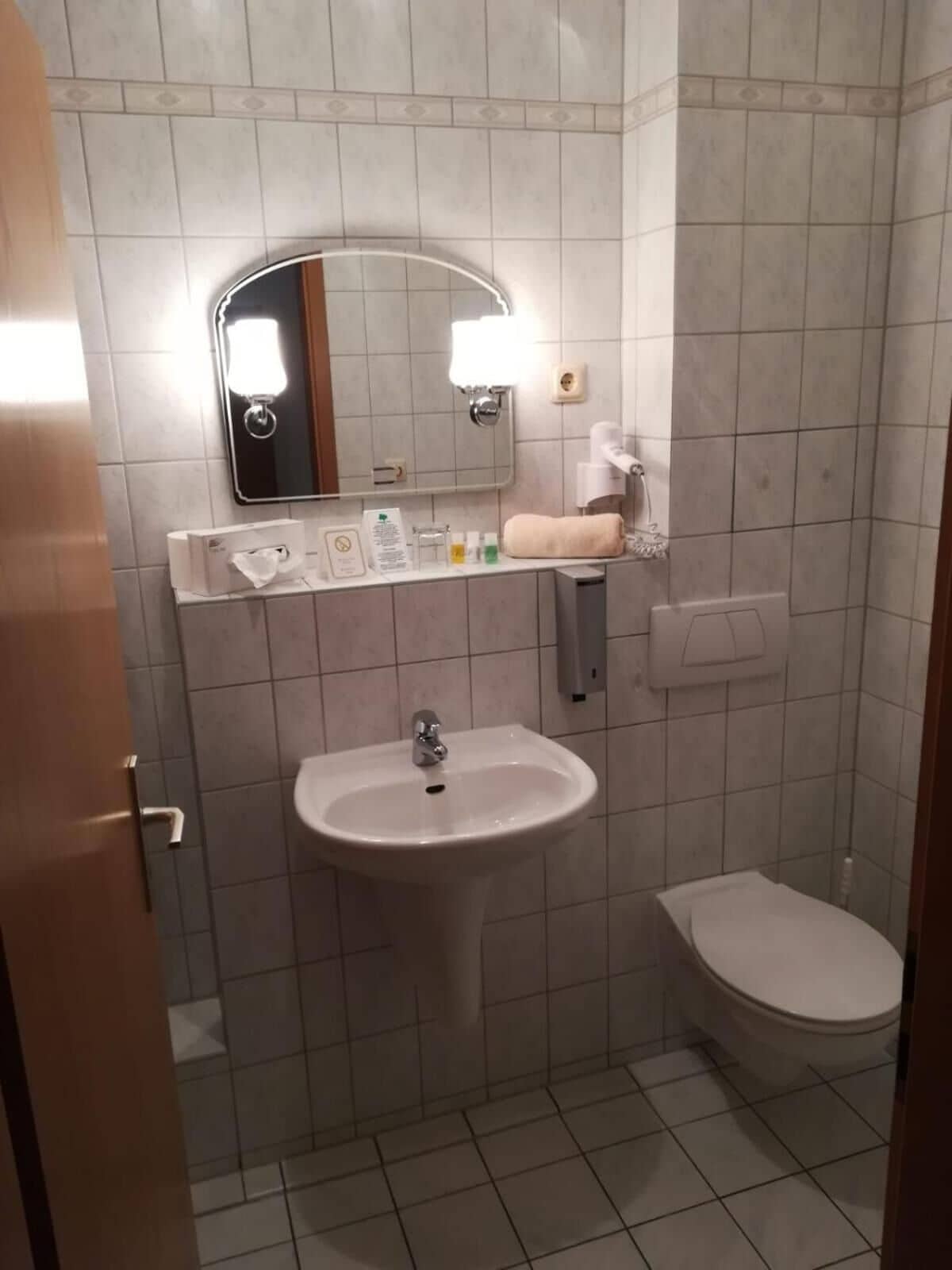 Et lille badeværelse med vask, toilet og spejl.