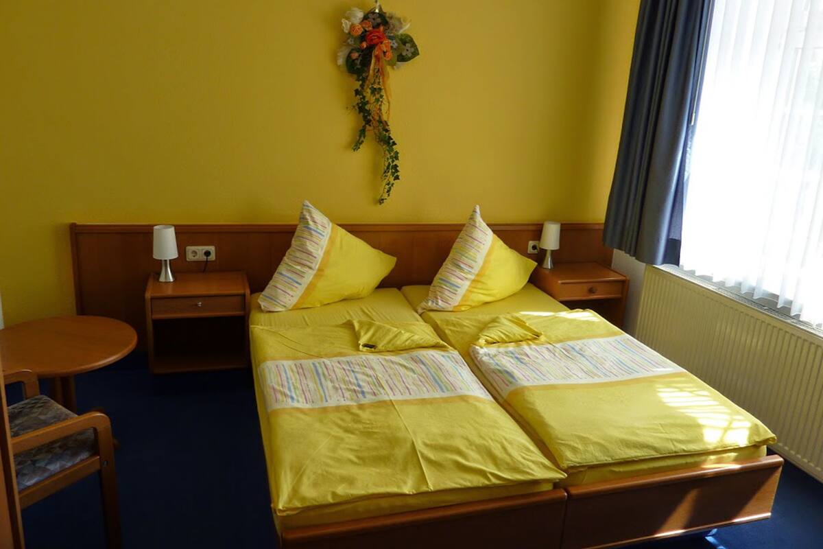 Ein Hotelzimmer mit einem Doppelbett, zwei Nachttischen, einem kleinen runden Tisch und einem Stuhl.