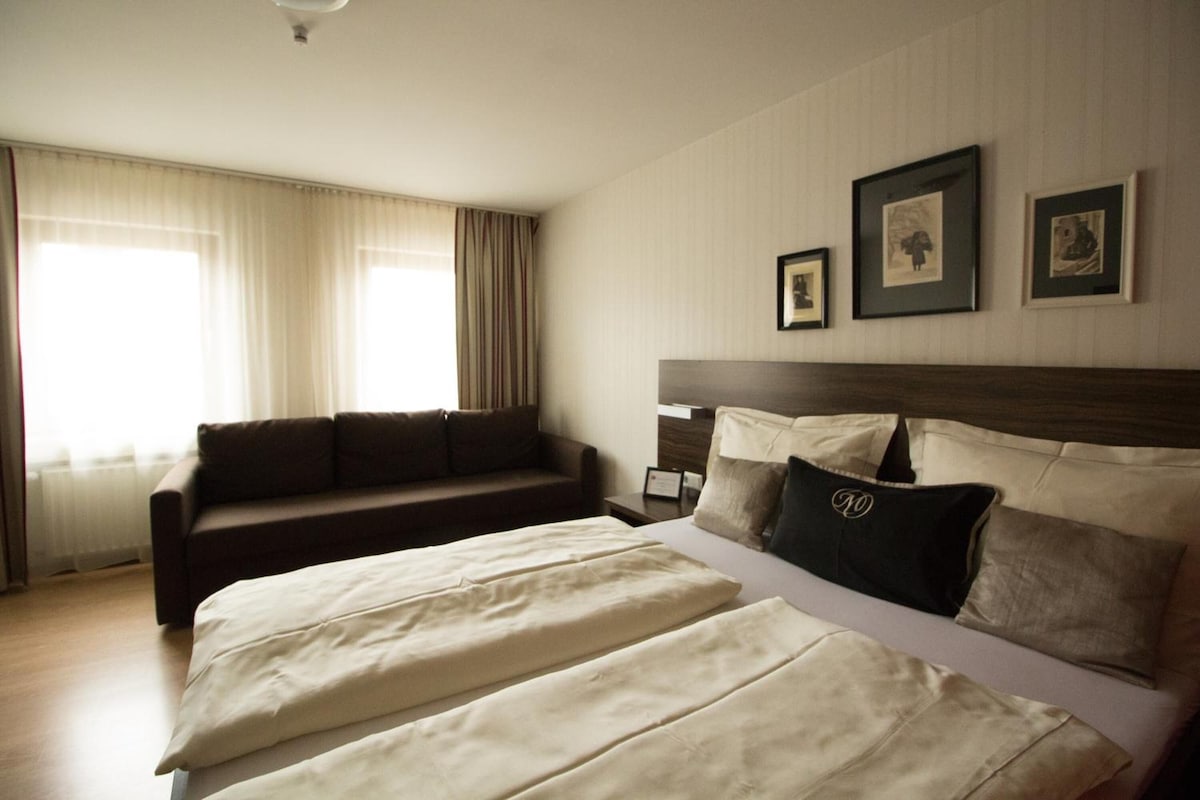 A hotel room with a large bed, a sofa, and a window with curtains.