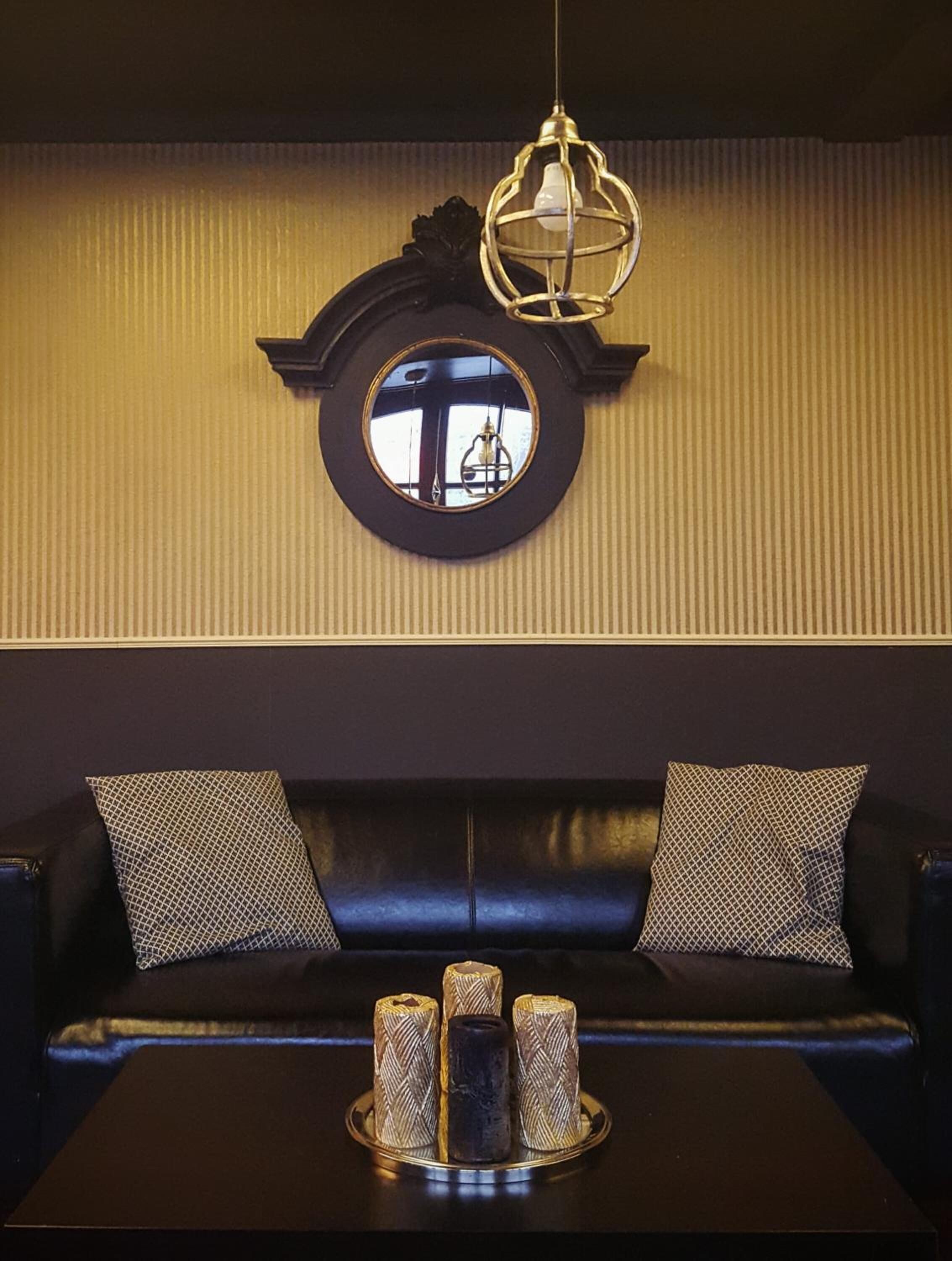 Um quarto com um espelho redondo, um sofá de couro preto e uma mesa com velas.