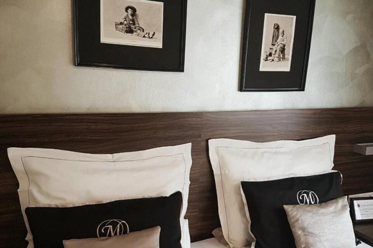 A bed with a headboard, two framed pictures on the wall above, and pillows with a monogram.