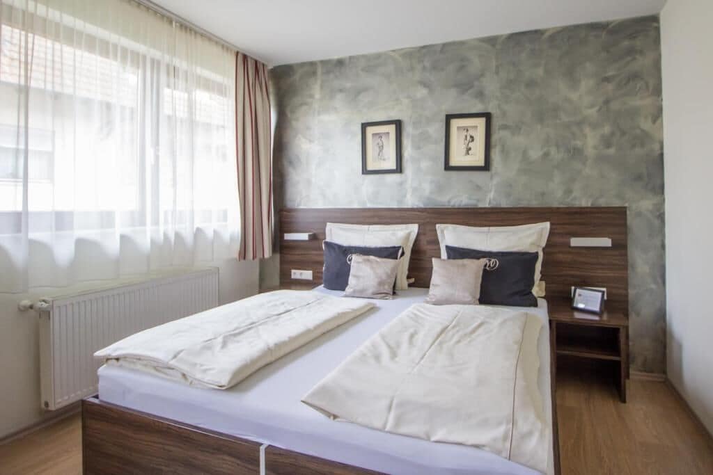 Un lit double avec du linge de lit blanc, une tête de lit en bois et deux tables de chevet avec une petite lampe.