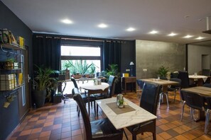 A restaurant with a tiled floor, multiple tables and chairs, potted plants, and a large window with curtains. - Landhotel Wolfschlugen (Wolfschlugen)