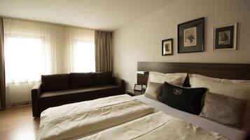 A hotel room with a large bed, a sofa, and two framed pictures on the wall.