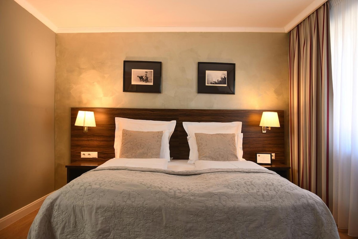 A hotel room with a large bed, two wall-mounted lamps, and two framed pictures on the wall.