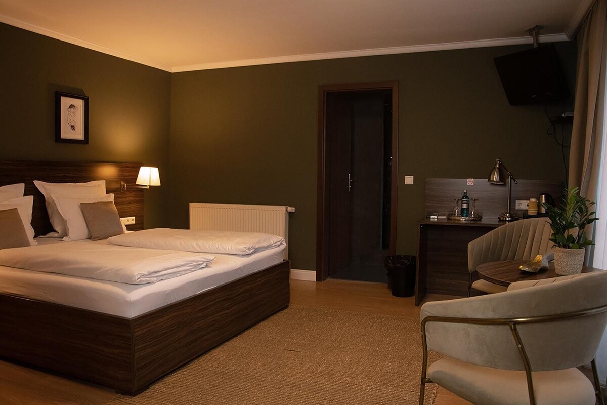 A hotel room with a large bed, a desk, a chair, and a television.