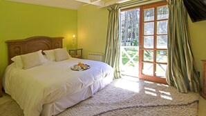 Un dormitorio con una cama grande, una mesita de noche, una lámpara y vistas a un jardín a través de una puerta corrediza.