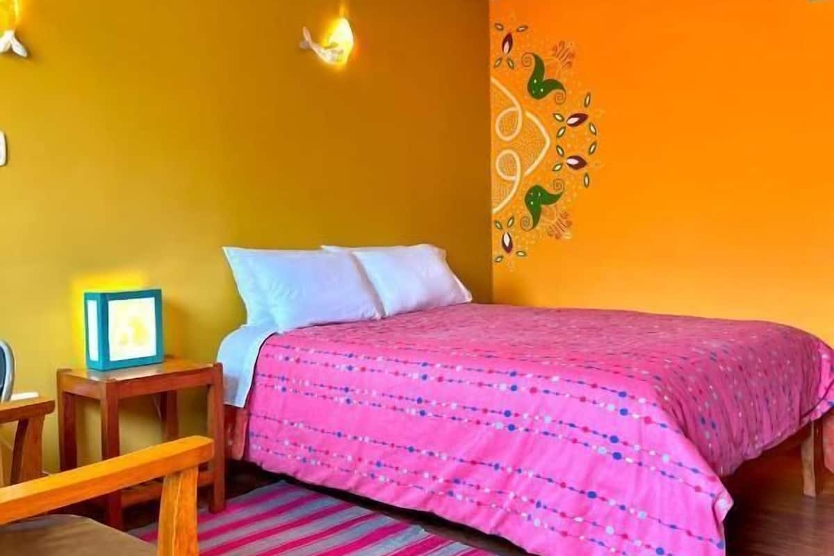A room with a bed, a wooden chair, a striped rug, and a wall with a decorative pattern.