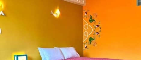 A room with a bed, a wooden chair, a striped rug, and a wall with a decorative pattern.