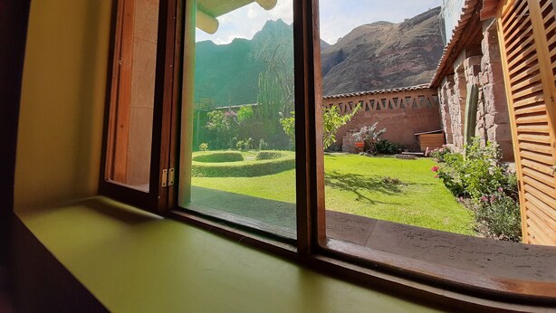 A window with a view of a courtyard, a wooden structure, and a mountain in the background. - Pisac Inca Guest House - Hostel (Pisac)
