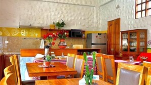 A dining area with wooden tables and chairs, a kitchen in the background, and a ceiling with wooden beams. - Pisac Inca Guest House - Hostel (Pisac)