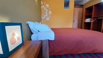 A hotel room with a bed, a wooden nightstand, a framed picture, a wardrobe, and a patterned carpet.