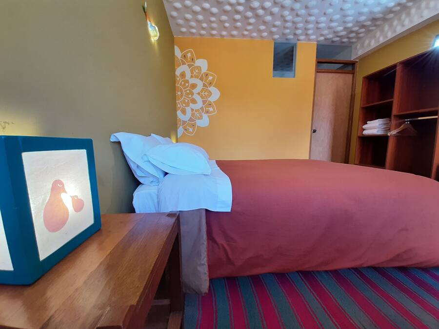 A hotel room with a bed, a wooden nightstand, a framed picture, a wardrobe, and a patterned carpet.