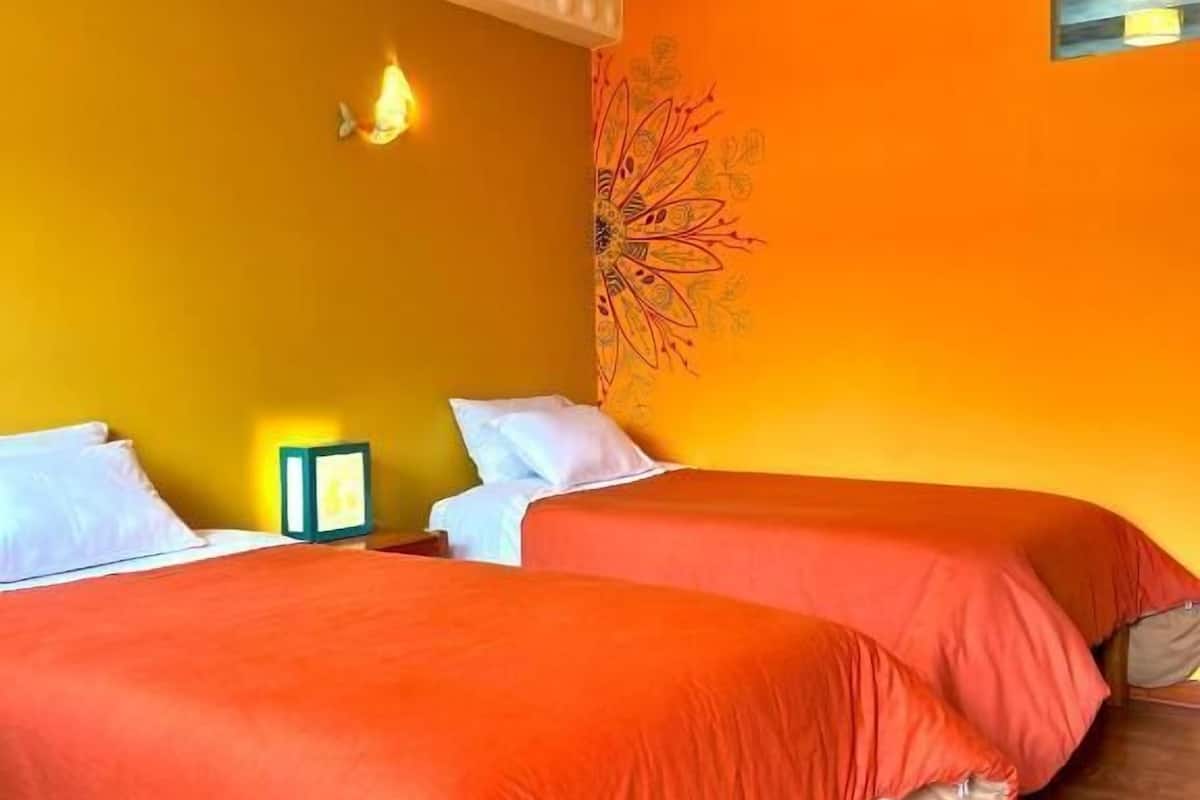 A room with two beds, wooden flooring, a wall with a floral tapestry, and a ceiling with a textured pattern.