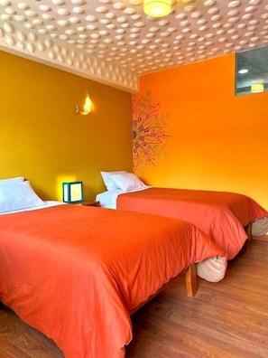 Habitación con dos camas, suelo de madera, una pared con un tapiz floral y un techo con textura.