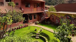 A two-story building with a red-tiled roof, surrounded by a well-maintained garden with various plants and flowers. - Pisac Inca Guest House - Hostel (Pisac)