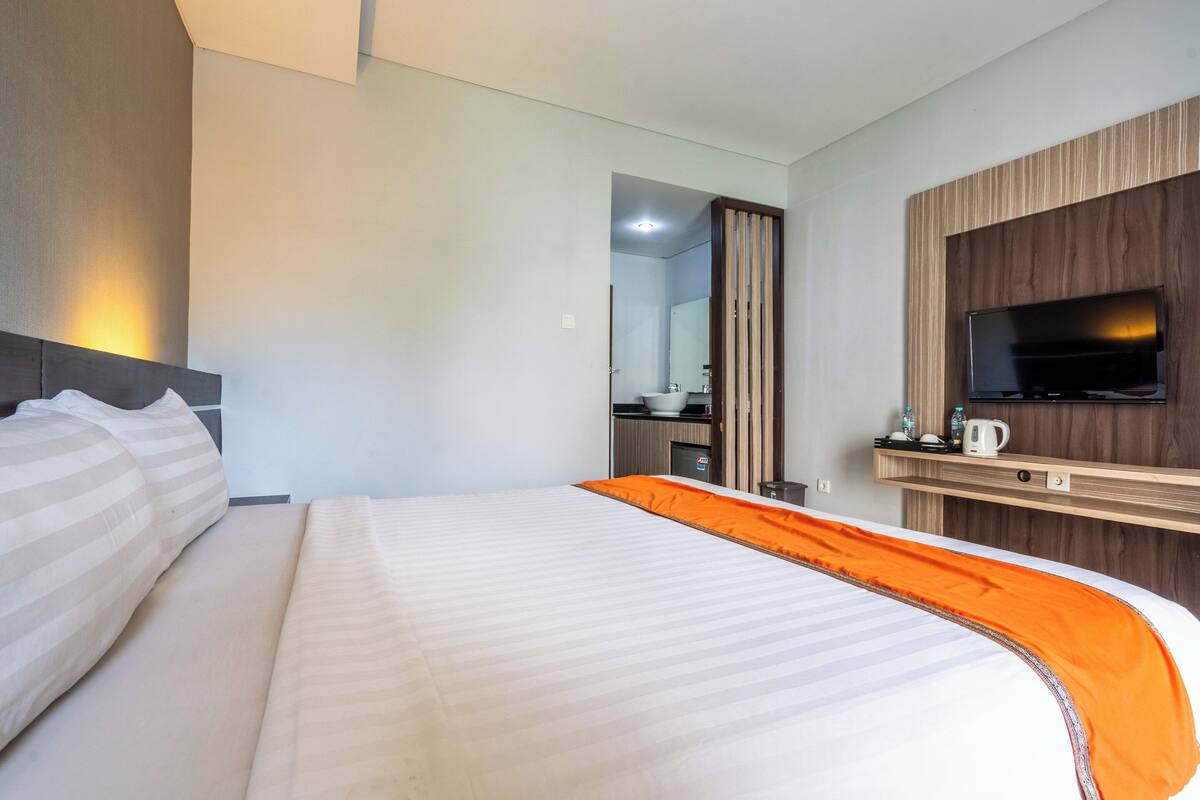 Une chambre d’hôtel avec un grand lit, un téléviseur fixé au mur et un petit coin cuisine.