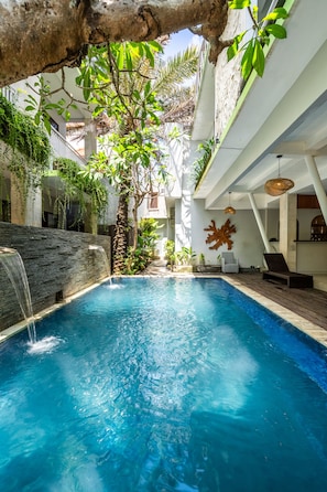 A swimming pool with a waterfall feature, surrounded by lush greenery and modern architecture.