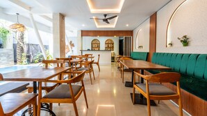 En modern restaurang med träbord och stolar, en grön, vadderad bänk och en takfläkt.