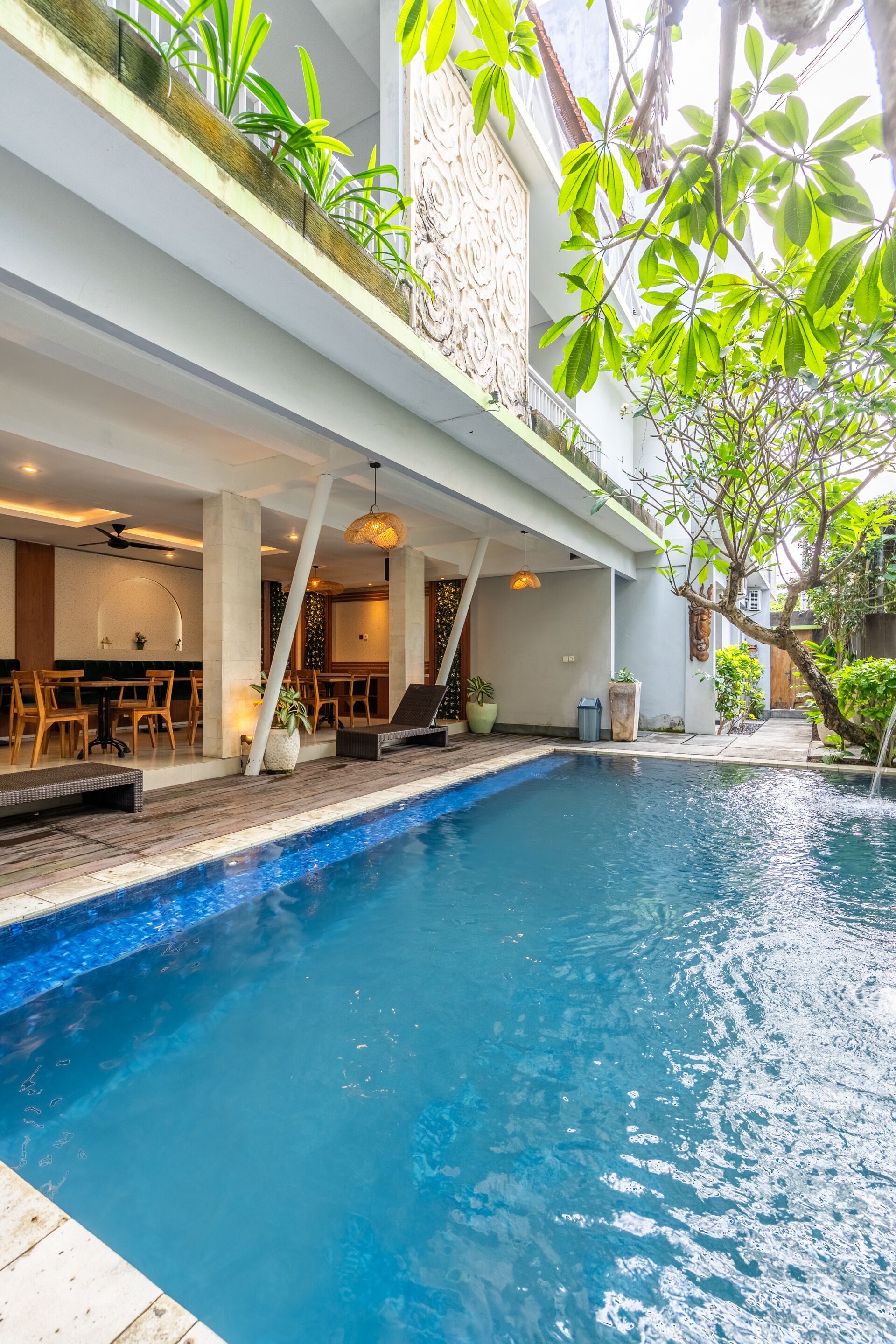 Ein Pool mit Holzterrasse, umgeben von Kübelpflanzen und einem Essbereich mit Holztischen und -stühlen.