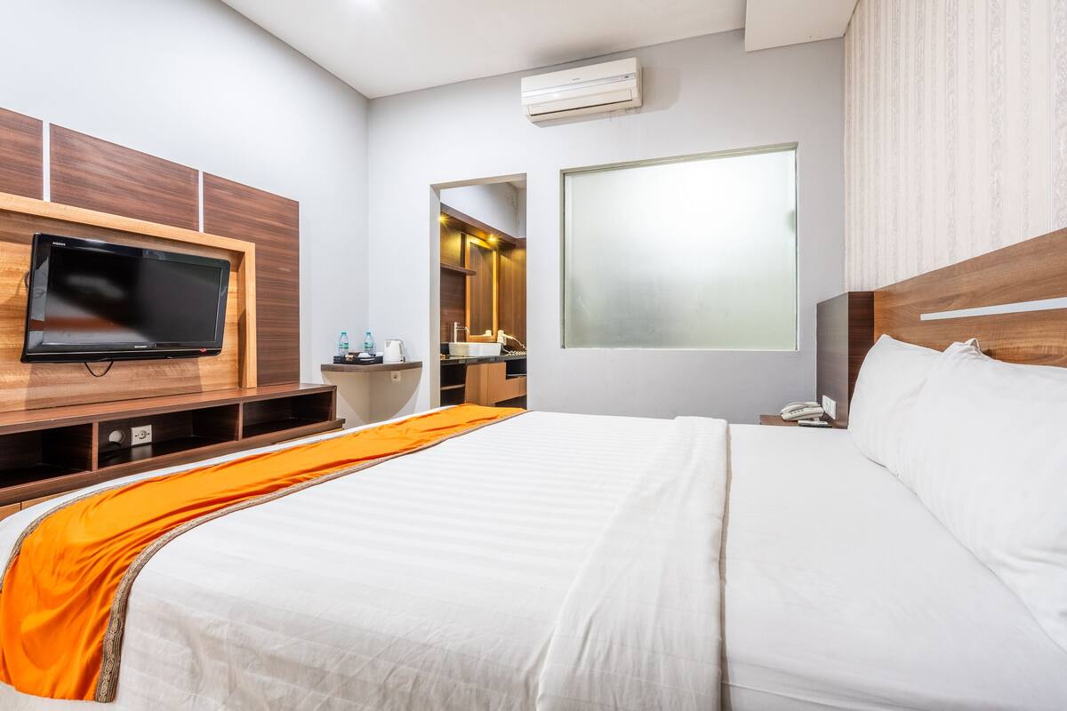 Une chambre d’hôtel avec un lit, un téléviseur fixé au mur, une salle de bain visible à travers une arche et une fenêtre à vitres dépolies.