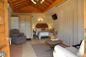 Una habitación de hotel con techo de madera, una cama con cabecera de madera, una silla, una mesa con fruta y un televisor en la pared.