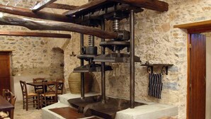 A rustic stone-walled room with a large mechanical press, wooden tables, and chairs. - Liotrivi Historical Mansion & Hotel (Monemvasia)