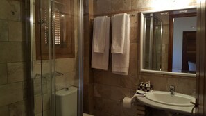 Un baño con cabina de ducha de vidrio, un inodoro, un lavamanos con espejo y dos toallas colgadas en la pared.