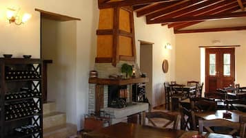 Un coin repas rustique avec des tables et des chaises en bois, une cheminée en briques et des étagères à vin.