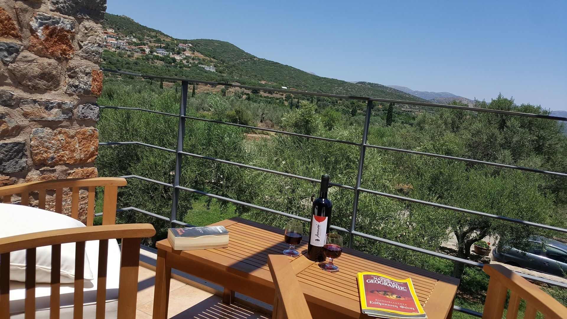 Ein Balkon mit Holztisch, einer Weinflasche und einem Buch mit dem Titel 'National Geographic'.